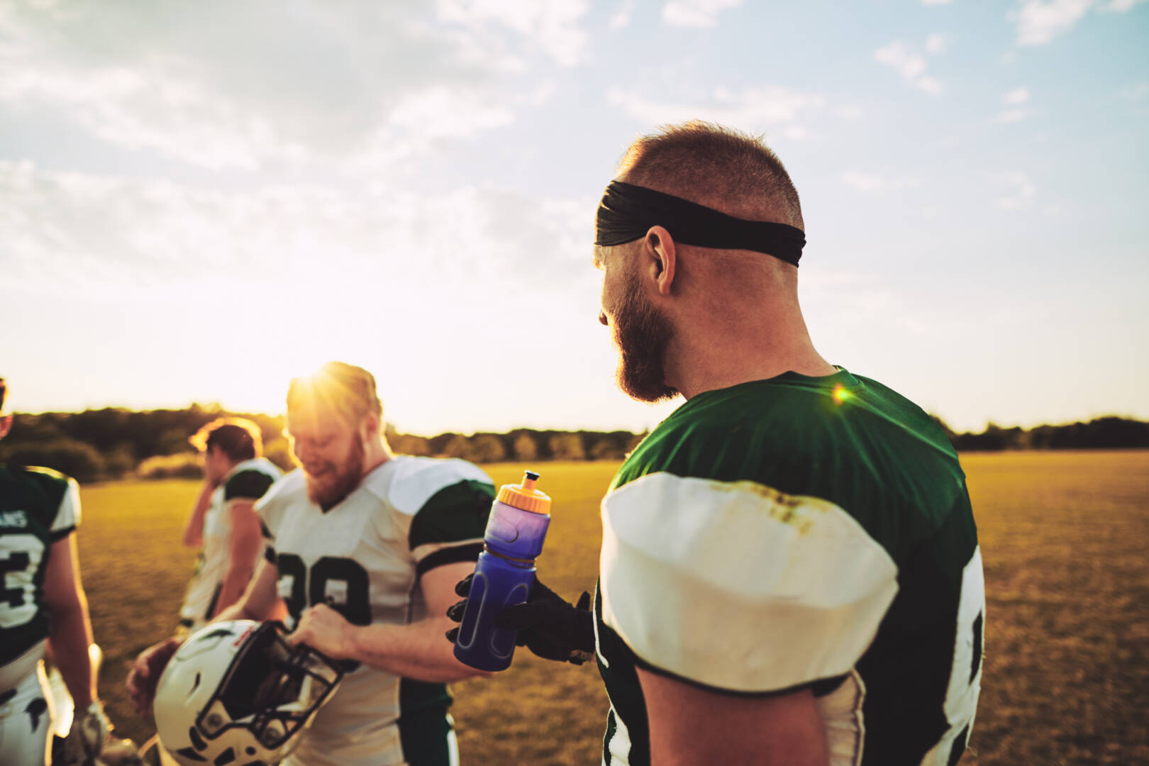 Team of young American football players talking together on a sports field after an afternoon practice